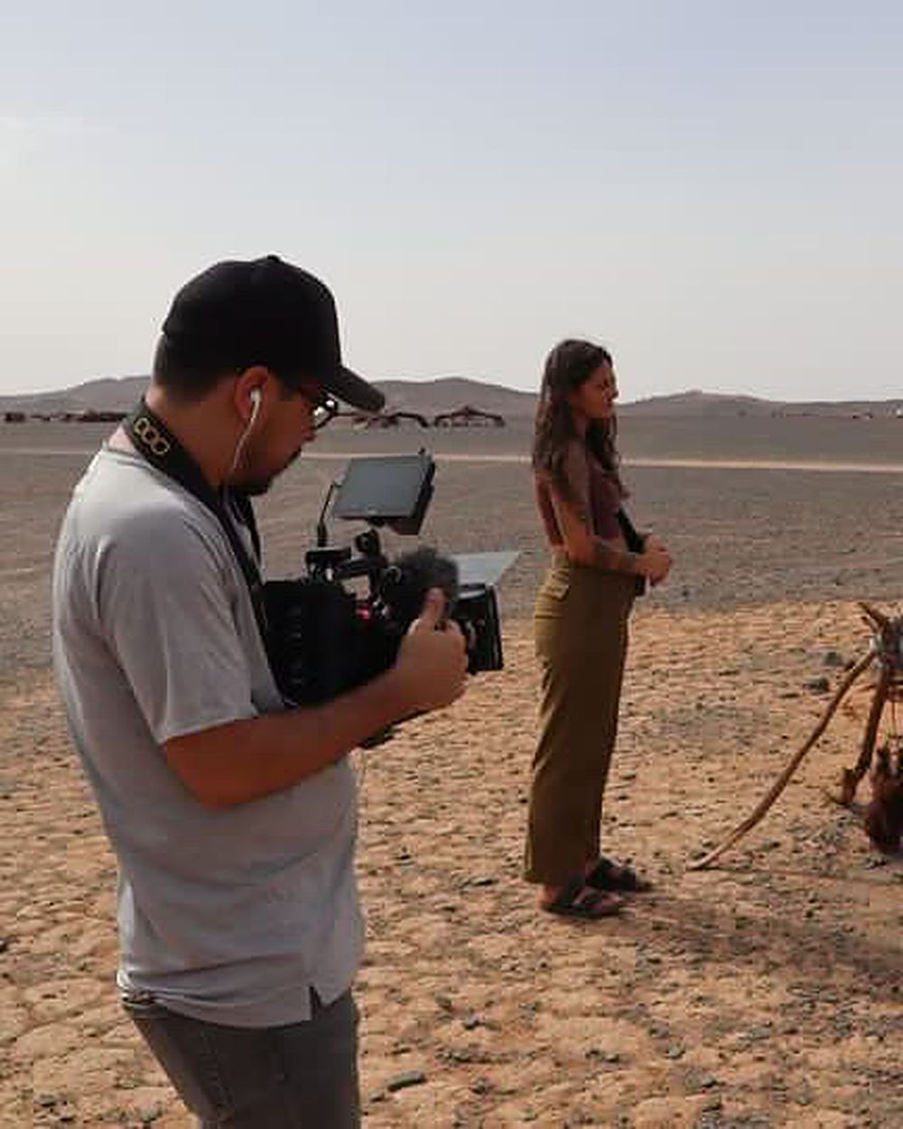 Rodaje en el desierto: un camarógrafo con cámara al hombro junto a una persona entrevistada